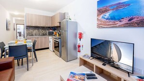 A modern kitchen with a dining area, a flat-screen TV, and a scenic coastal view.