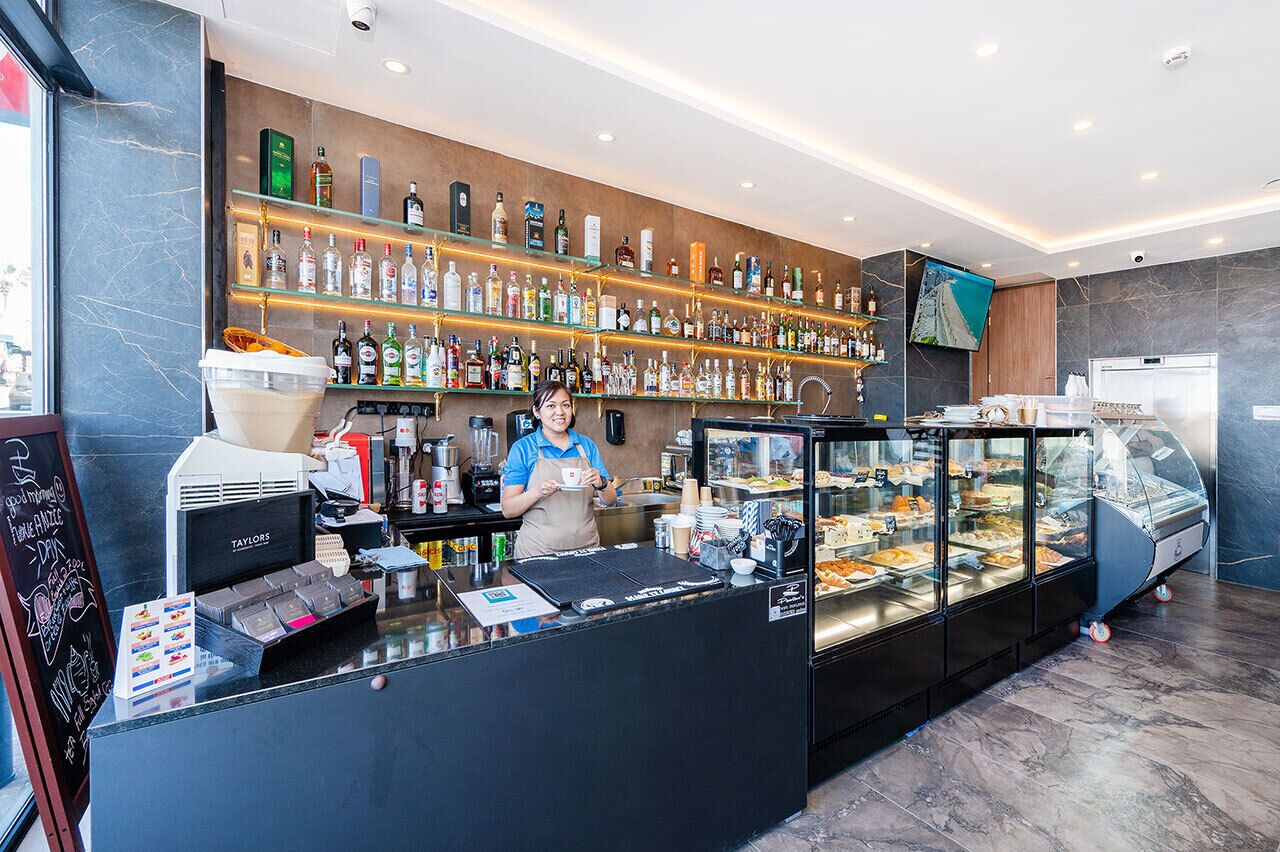 A modern bar area with a variety of liquor bottles on shelves, a coffee machine, and a display case with pastries.