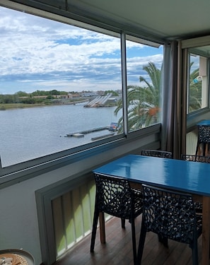 Quarto com uma grande janela com vista para um rio, uma mesa, cadeiras e um radiador.