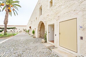 A cobblestone pathway leading to a row of stone buildings with arched doorways and a palm tree. - Cosy flat, ideal for 4px (Tavira)