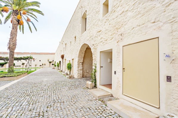 A cobblestone pathway leading to a row of white buildings with arched doorways and a palm tree on the left. - Cosy flat, ideal for 4px (Tavira)
