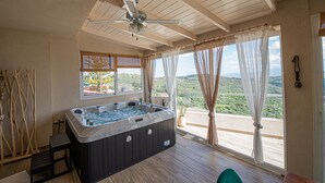 Ein Whirlpool in einem Zimmer mit Holzboden, Deckenventilator und großen Fenstern mit Vorhängen.