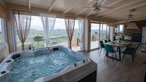 Ein Whirlpool in einem geräumigen Zimmer mit Blick auf die Landschaft, ein Essbereich mit Stühlen und Deckenventilatoren.