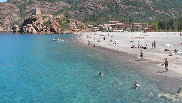 A beach with clear blue water, people sunbathing, and buildings in the background. - Appartement 2 en Pierre (Ota)