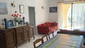 A dining area with a table covered in a patterned tablecloth, wooden chairs, a red sofa, and a cabinet with decorative items. - Appartement 2 en Pierre (Ota)