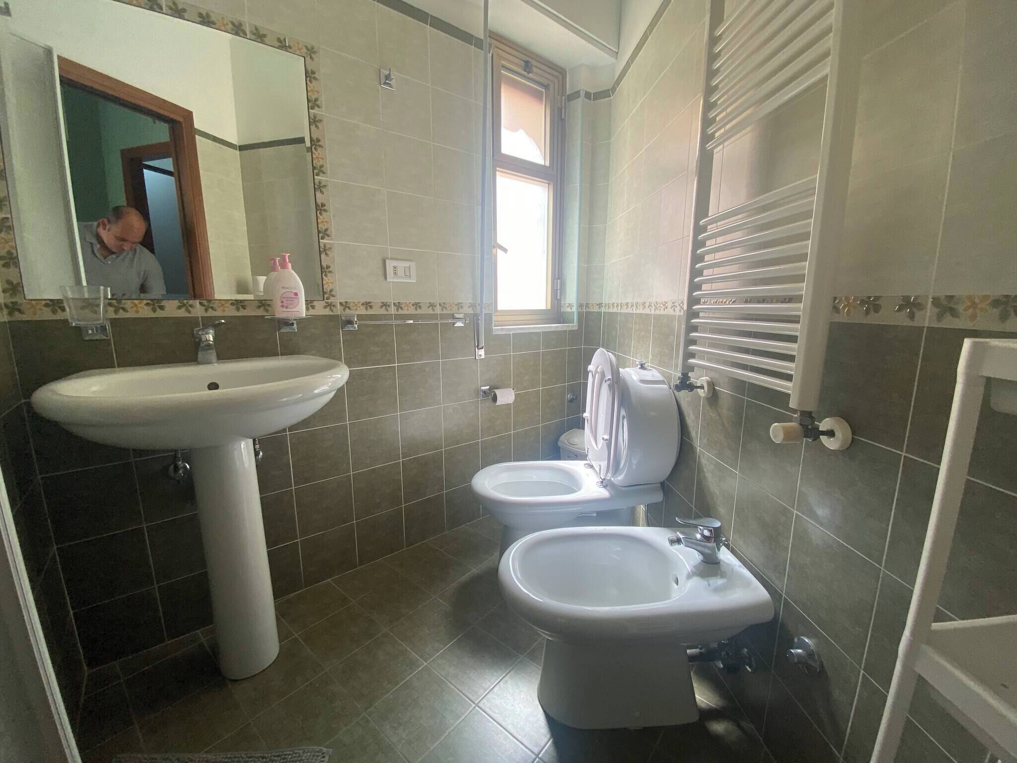 A bathroom with a sink, two toilets, a mirror, and a window.