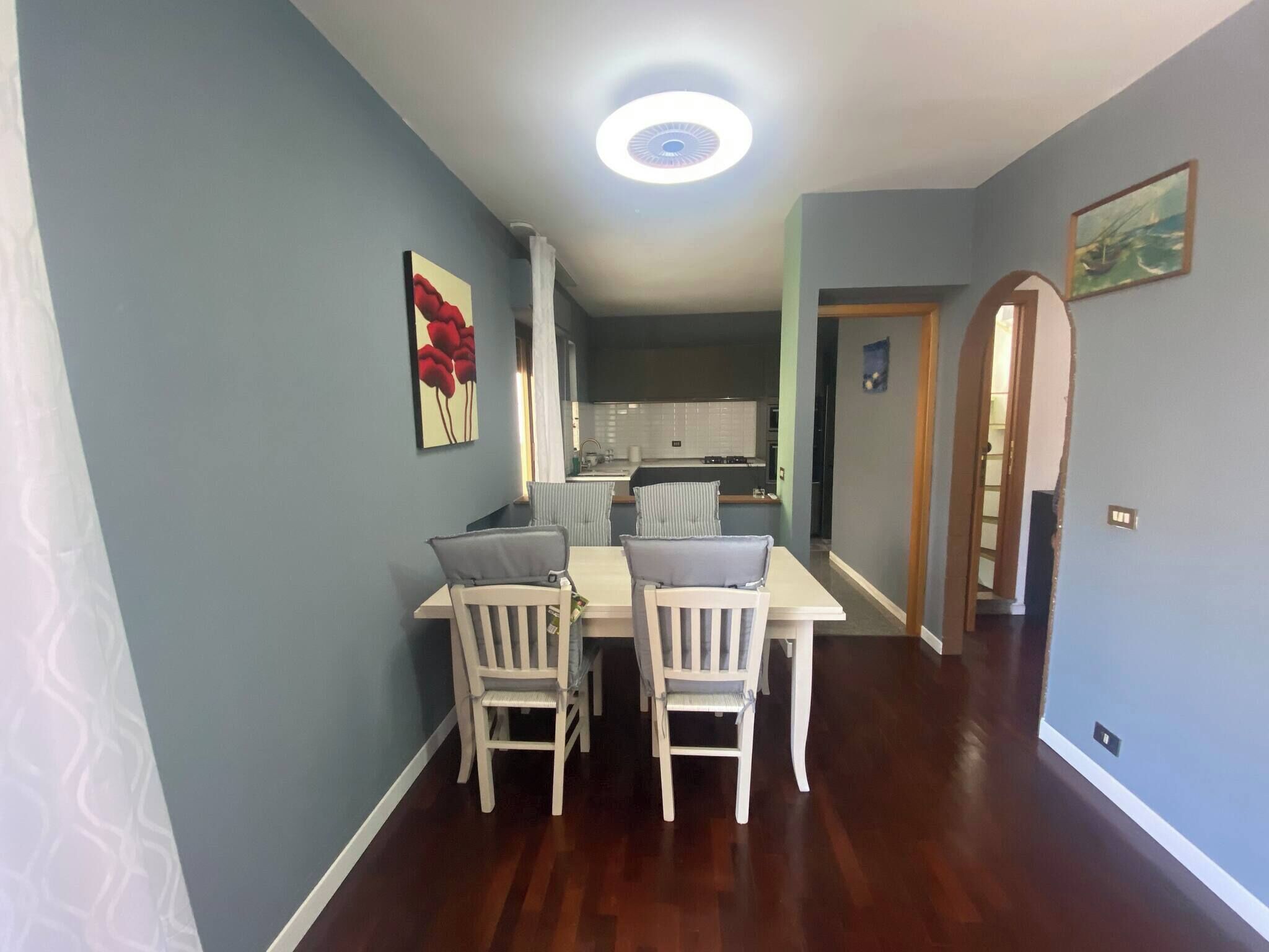 A dining area with a white table and chairs, a ceiling light, and a kitchen in the background.