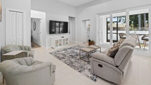 A modern living room with a flat-screen TV, grey sofas, a coffee table, and a large window offering a view of the outdoors. - Sunset Estate near Venice Beach (Venice)