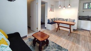Una sala de estar con sofá, una mesa de centro de madera, una mesa de comedor con bancos y una zona de cocina con lavamanos y encimera.