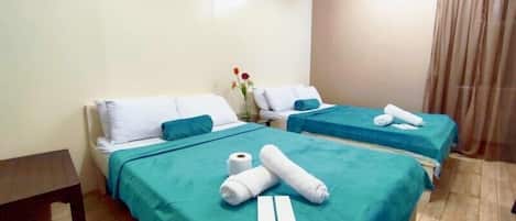 A hotel room with two beds, each with a teal bedspread and white pillows. There are towels and a roll of toilet paper on the beds.