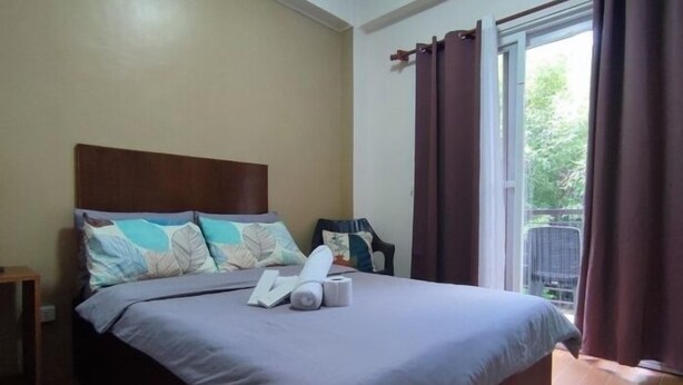 Una cama bien hecha con cabecera, una mesita de noche con lámpara y una ventana con cortinas.