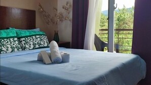 Una cama bien hecha con una colcha azul, una almohada de estampado verde y blanco, y un jarrón con flores secas.