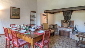 Un comedor con una mesa de madera dispuesta para cuatro personas, rodeada de sillas rojas. En la pared, se ve una estantería con libros y un cuadro enmarcado.