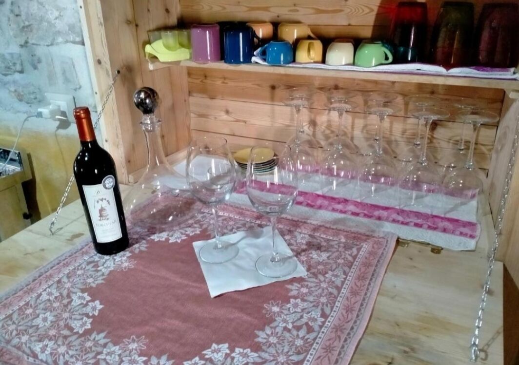Ein Weinkühler aus Holz mit bunten Tassen und einer Weinflasche auf einem Tisch mit Blumenmuster.