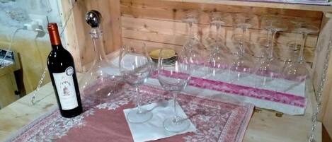 Ein Weinkühler aus Holz mit bunten Tassen und einer Weinflasche auf einem Tisch mit Blumenmuster.