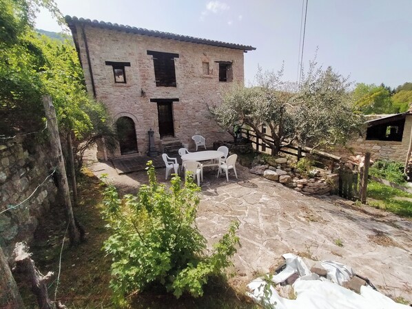 A stone building with a patio area featuring a table and chairs. - Maison en Pierre (Fiastra)