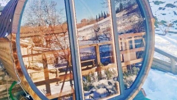 Una gran estructura cilíndrica transparente con interior de madera, que refleja un paisaje nevado y árboles.