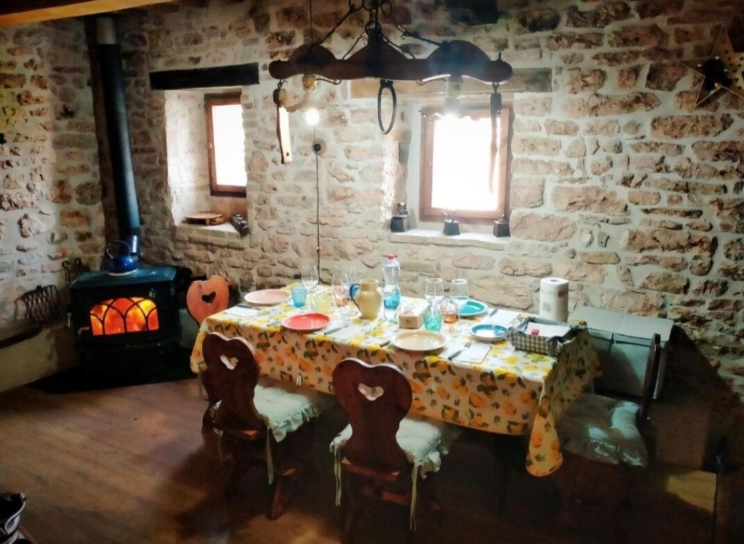 Ett rustikt matrum med en vägg av natursten, en vedeldad kamin och ett bord dukat för fyra personer.