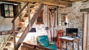 Un interior rústico con una escalera de madera, paredes de piedra, un sofá de cuero, un sillón color turquesa y una mesa de madera con un televisor.