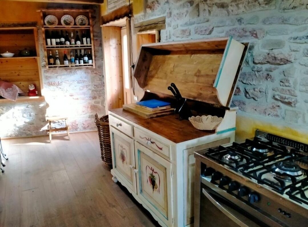 Une cuisine rustique avec un îlot central en bois, une cuisinière à gaz et des étagères remplies de bouteilles.
