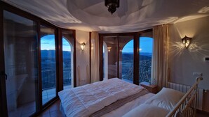A bedroom with a large bed, two wall sconces, a ceiling light, and a view of the landscape through large sliding doors. - Spectacular mountain views in a romantic location. Close to Mojacar beaches. (Turre)