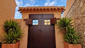 A brown wooden double door with decorative metalwork, flanked by two potted plants, set against a stucco wall with a tiled roof. - Spectacular mountain views in a romantic location. Close to Mojacar beaches. (Turre)
