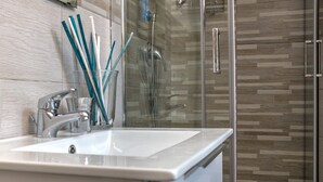 A bathroom with a white sink, a glass shower enclosure, and a wooden-patterned wall. - Holiday House Manuela Apartments 1 Piazza del Plebiscito (CENTRO)