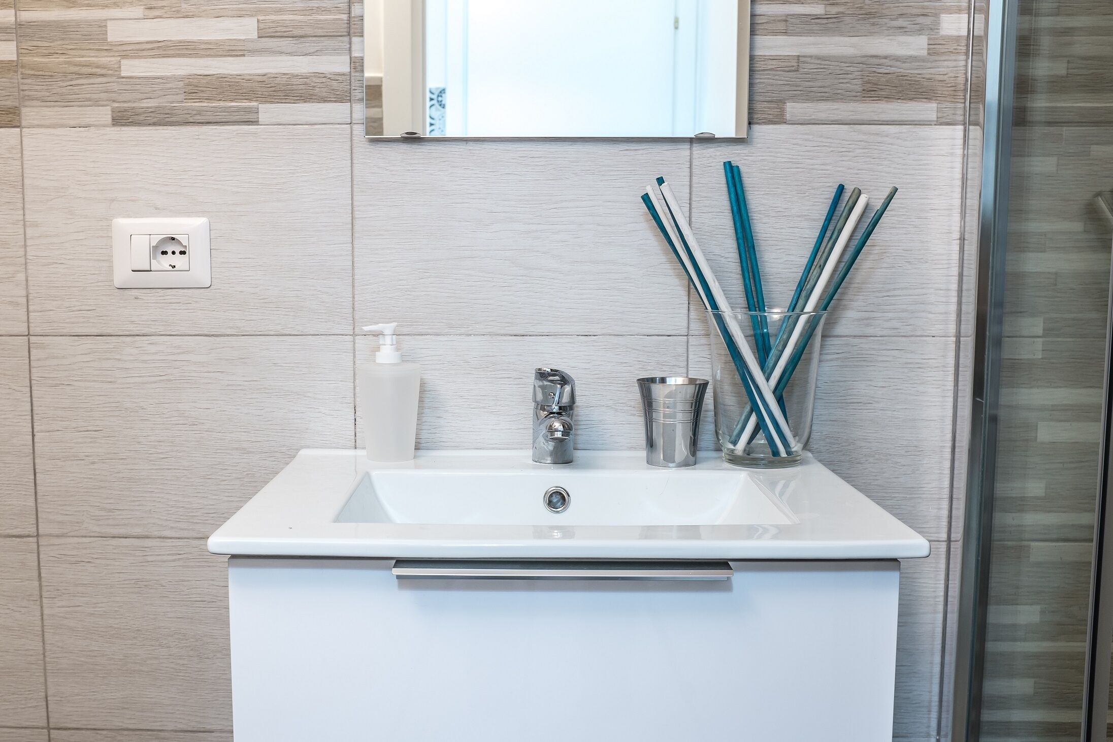 A modern bathroom with a white sink, a mirror, and a glass container holding toothbrushes.