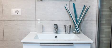 A modern bathroom with a white sink, a mirror, and a glass container holding toothbrushes.