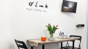 A dining area with a table set for two, a TV mounted on the wall, and a wall decoration with cooking utensils and the phrase "Enjoy Cooking Time". - Holiday House Manuela Apartments 1 Piazza del Plebiscito (CENTRO)