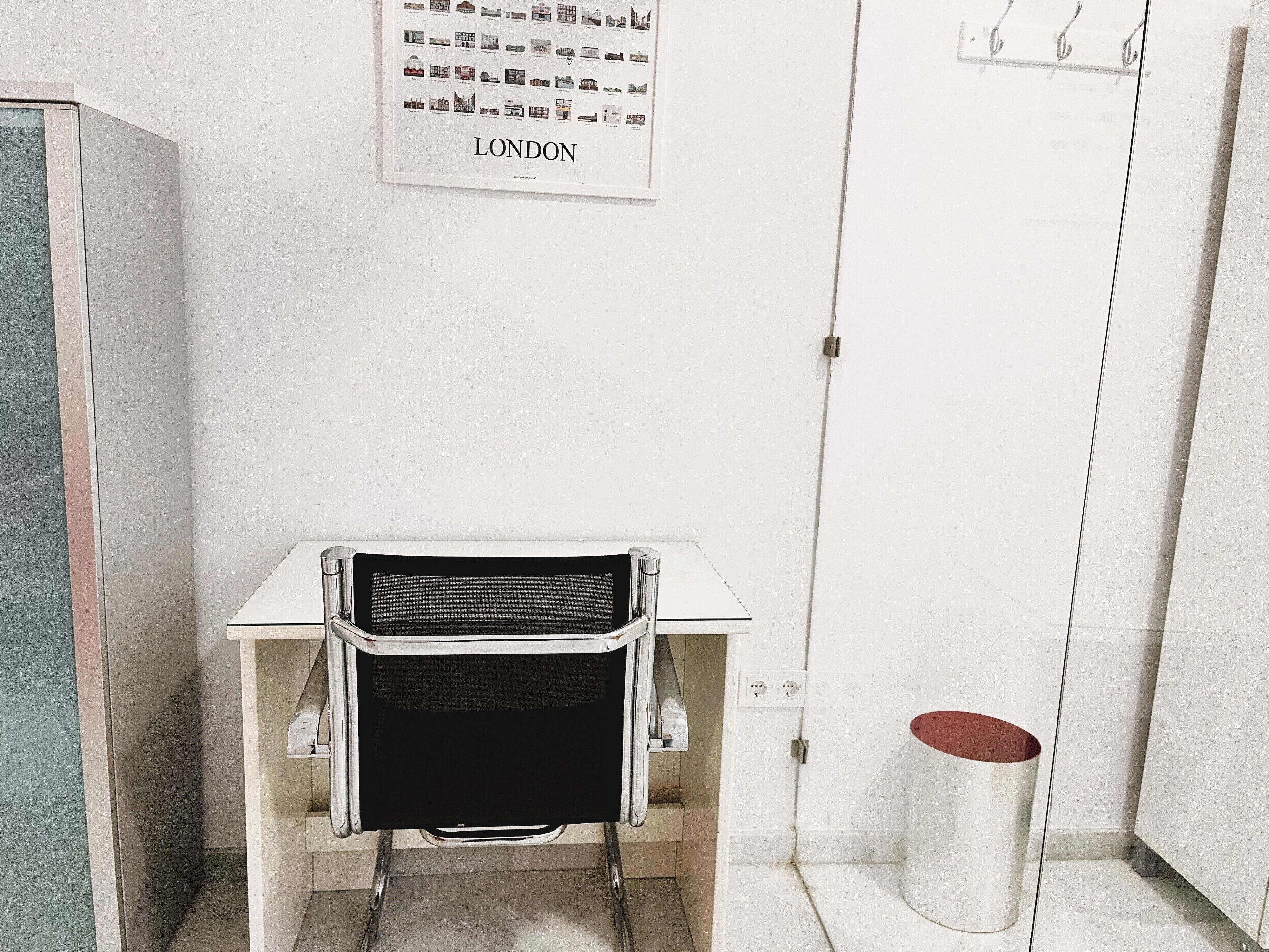 A modern, minimalist bathroom with a white sink, a black chair, and a framed picture of London on the wall.