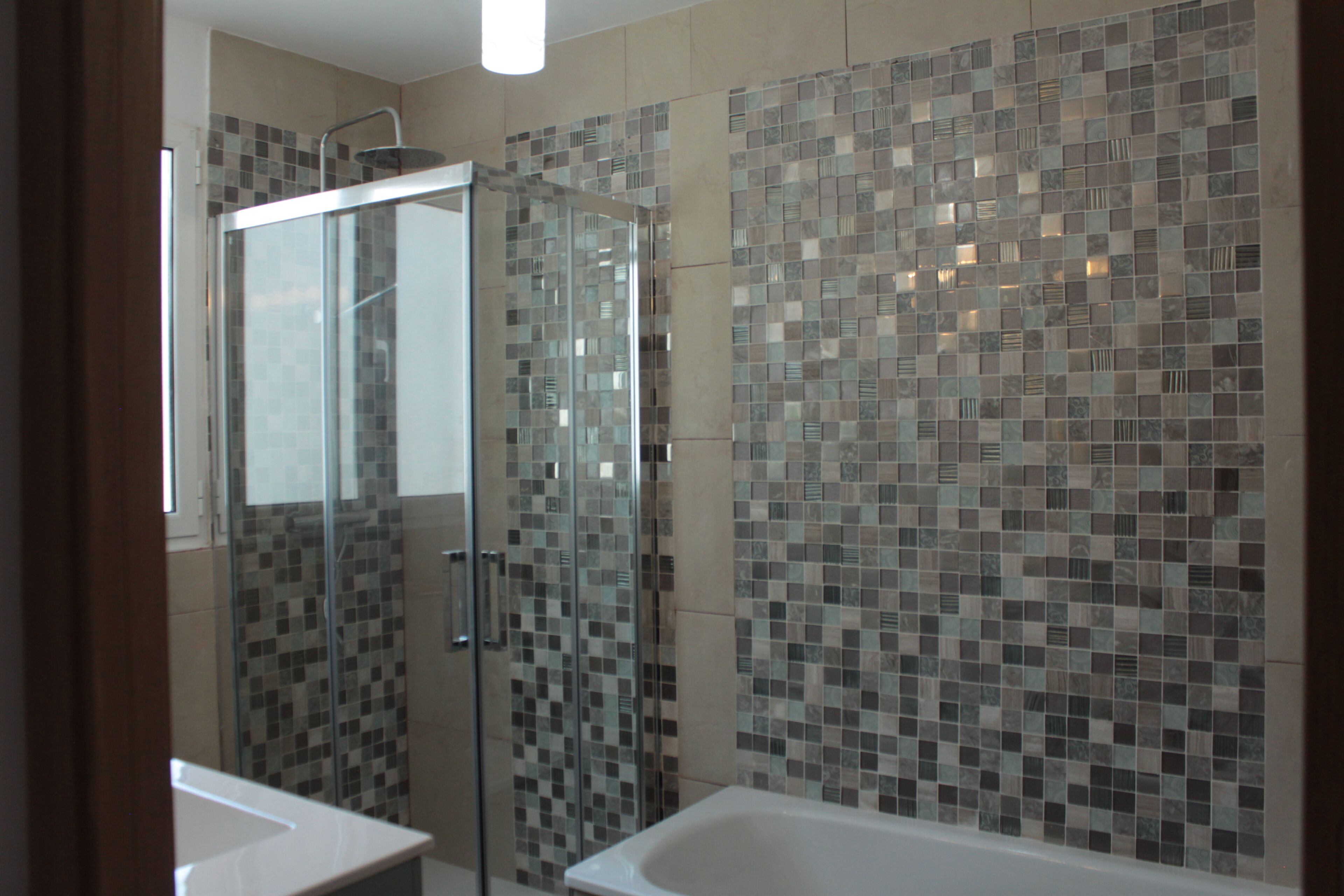 Une salle de bain dotée d’une douche à parois de verre, d’un mur recouvert d’une mosaïque et d’une baignoire blanche.