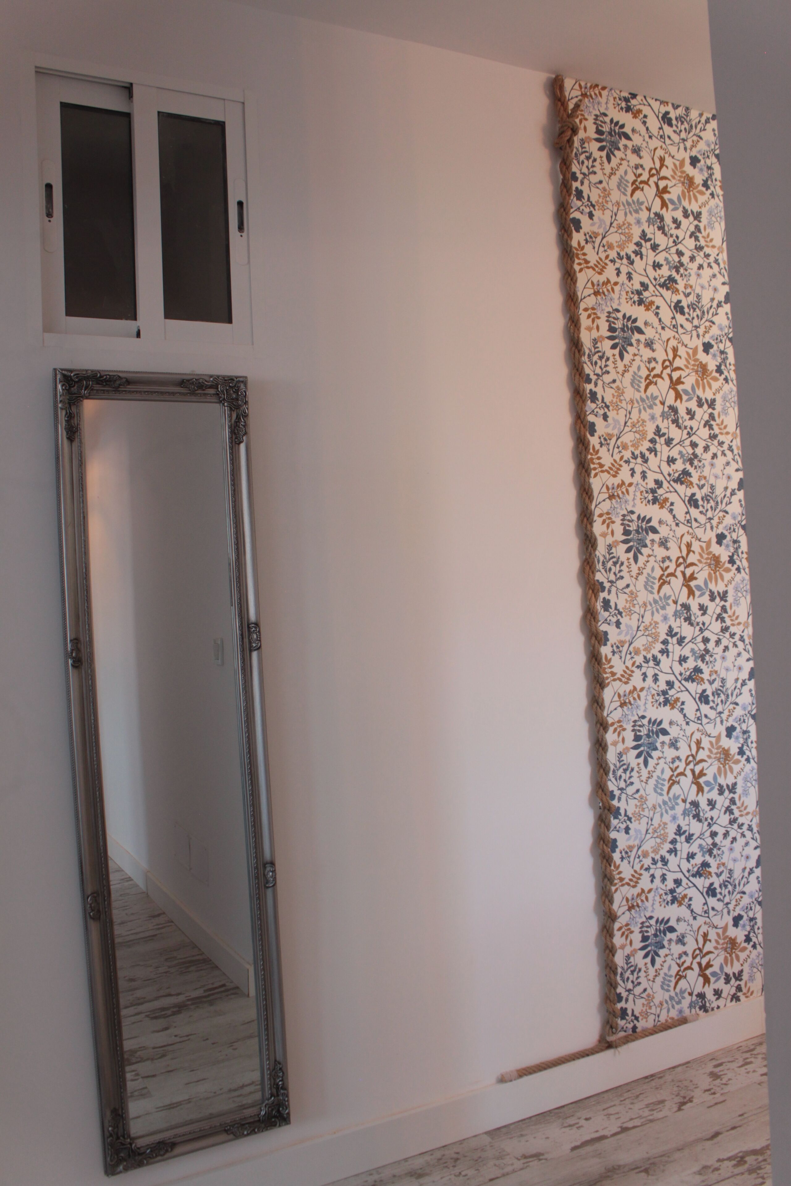 Een kamer met een grote spiegel, een raam met gezandstraald glas en een wand met een bloemenprint.