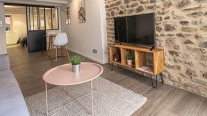 Una sala de estar moderna con una pared de piedra, un televisor de pantalla plana sobre un soporte de madera, un sofá gris, una mesa de centro redonda con una planta y un suelo de madera.