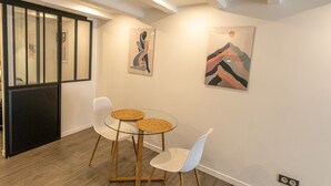 Un comedor con una mesa redonda y dos sillas, un separador negro y obras de arte en las paredes.
