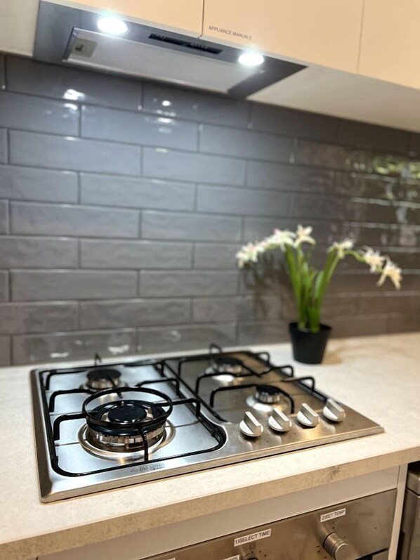 A kitchen with a gas stove, a backsplash of gray tiles, and a potted plant.