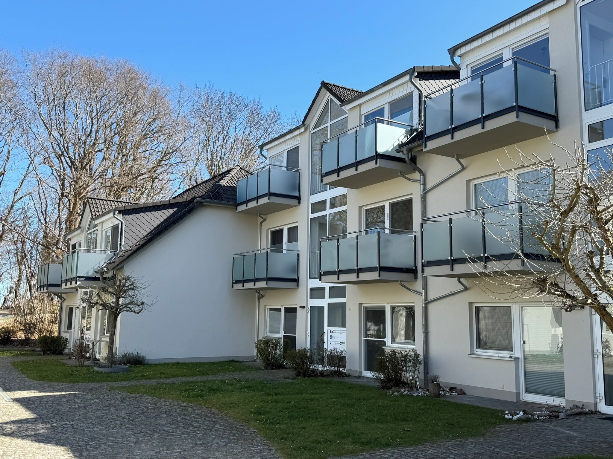 En flervåningsbostadsbyggnad med balkonger, en asfalterad uppfart och en gräsyta.