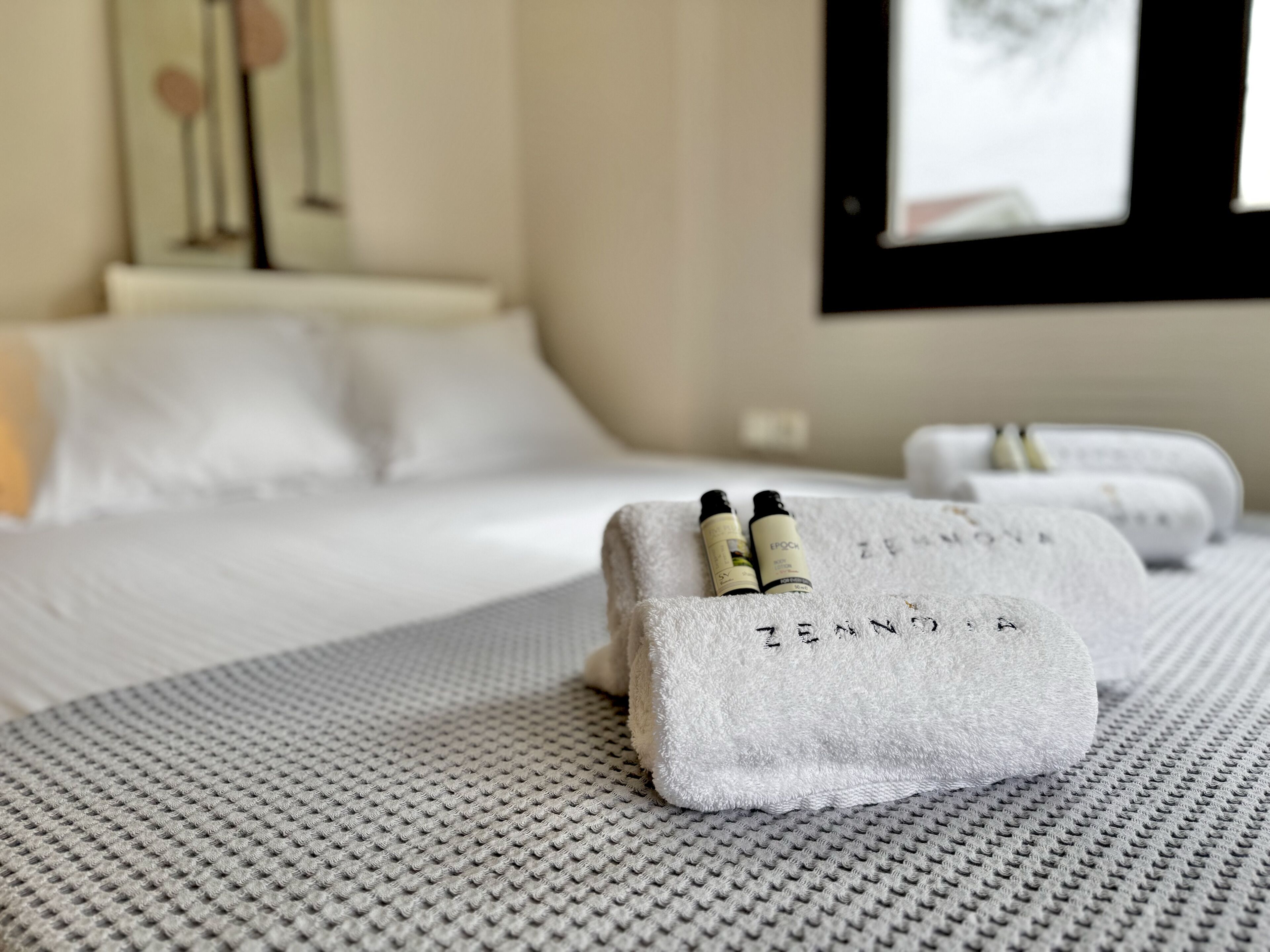 A neatly made bed with white linens and two small, gray, textured bags on the bed.