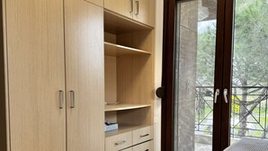 Una habitación con un armario de madera, un ventanal corredero que da a un espacio al aire libre y una cama con cubrecama estampado.