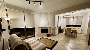 Una sala de estar con sofá, chimenea, comedor con mesa y sillas, y área de cocina con refrigerador.