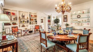 A dining area with a round table, chairs, a chandelier, and bookshelves filled with books and decorative items. - Villa Elide with private pool (Massa Lubrense)