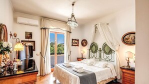 A bedroom with a bed, a chandelier, a dresser, and a window with curtains. - Villa Elide with private pool (Massa Lubrense)