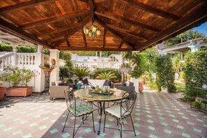 Un patio al aire libre con techo de madera, una mesa redonda con sillas y plantas en macetas.