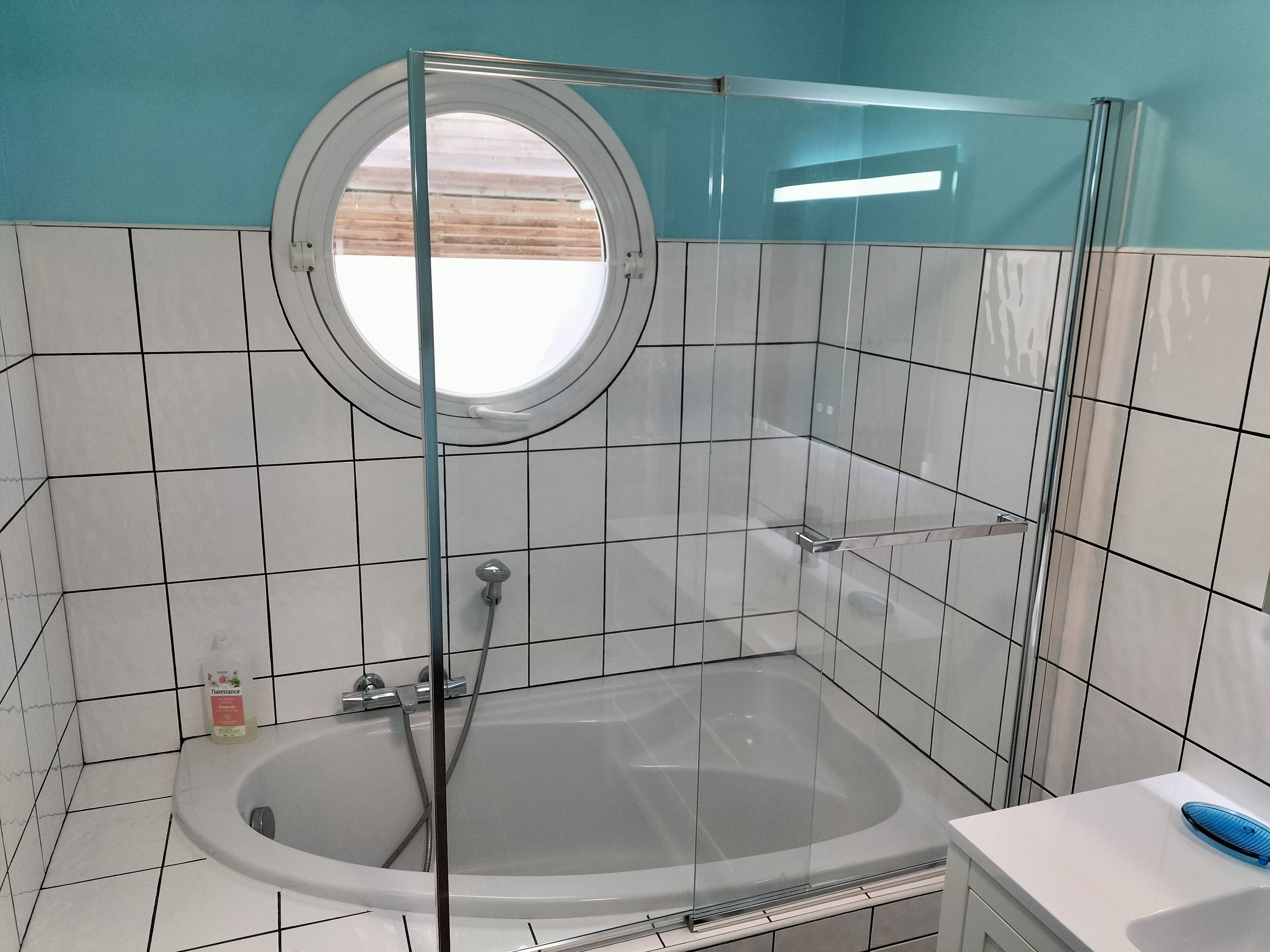 Ein Badezimmer mit einer Badewanne, einer Glaskabine zur Dusche und einem runden Fenster.