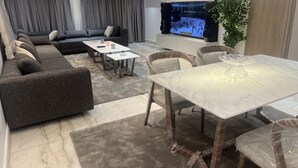 A modern living room with a sectional sofa, a dining table with chairs, a flat-screen TV, and a potted plant. - Saif City Stars  (محافظة القاهرة‬)
