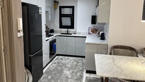 A modern kitchen with white cabinets, a black refrigerator, a built-in oven, and a small window. - Saif City Stars  (محافظة القاهرة‬)