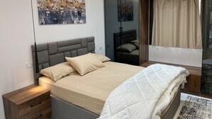 A modern bedroom with a large bed, a nightstand, a mirror, and abstract art on the wall. - Saif City Stars  (محافظة القاهرة‬)
