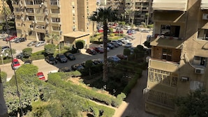 A multi-story residential building with balconies, air conditioning units, and a parking area with several cars. - Saif City Stars  (محافظة القاهرة‬)