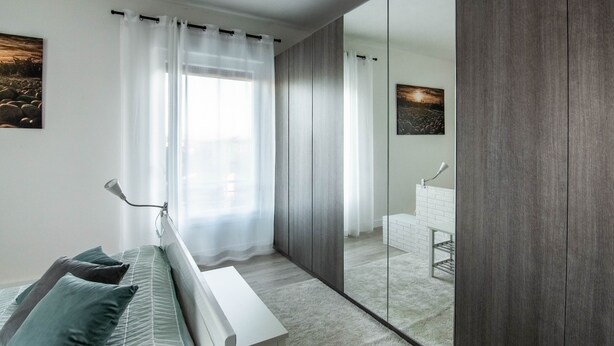 A modern bedroom with a bed, a bedside table, a mirror, and a view of a bathroom through a sliding door.