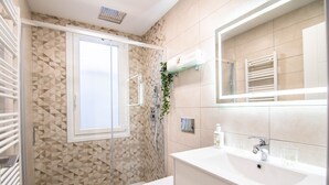 A modern bathroom with a geometric tile backsplash, a glass shower enclosure, a white sink with a mirror above it, and a towel rack.